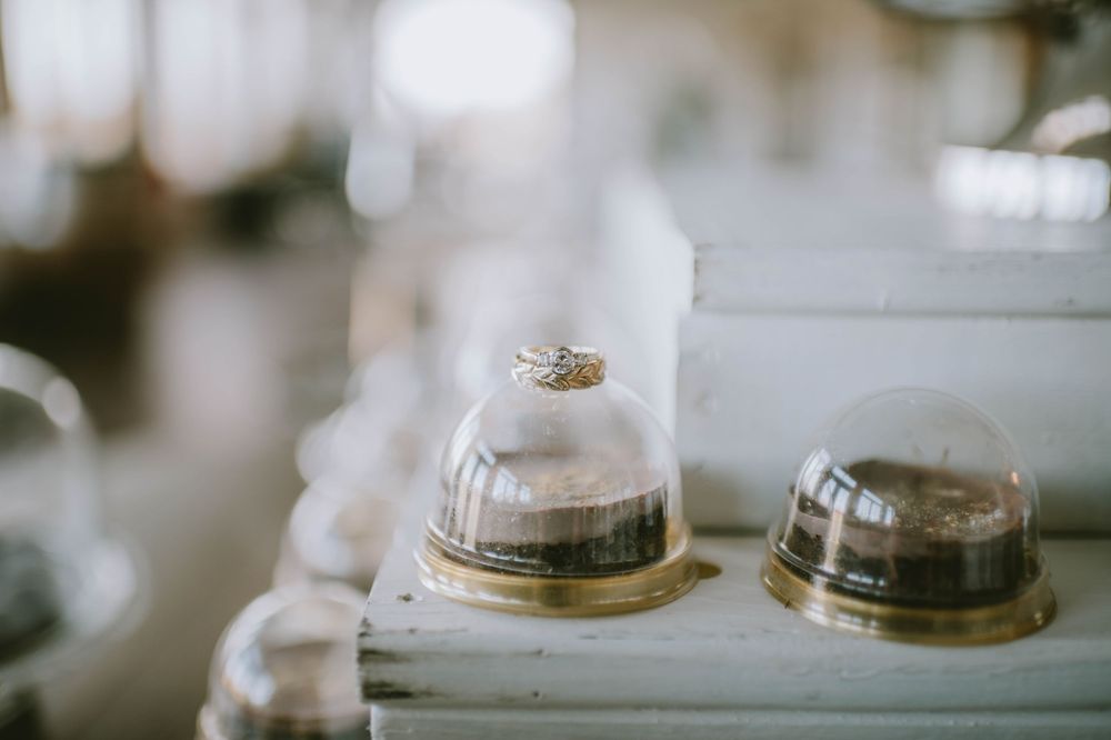 Gold wedding rings displayed under glass domes on a white surface, with soft bokeh background lighting.
