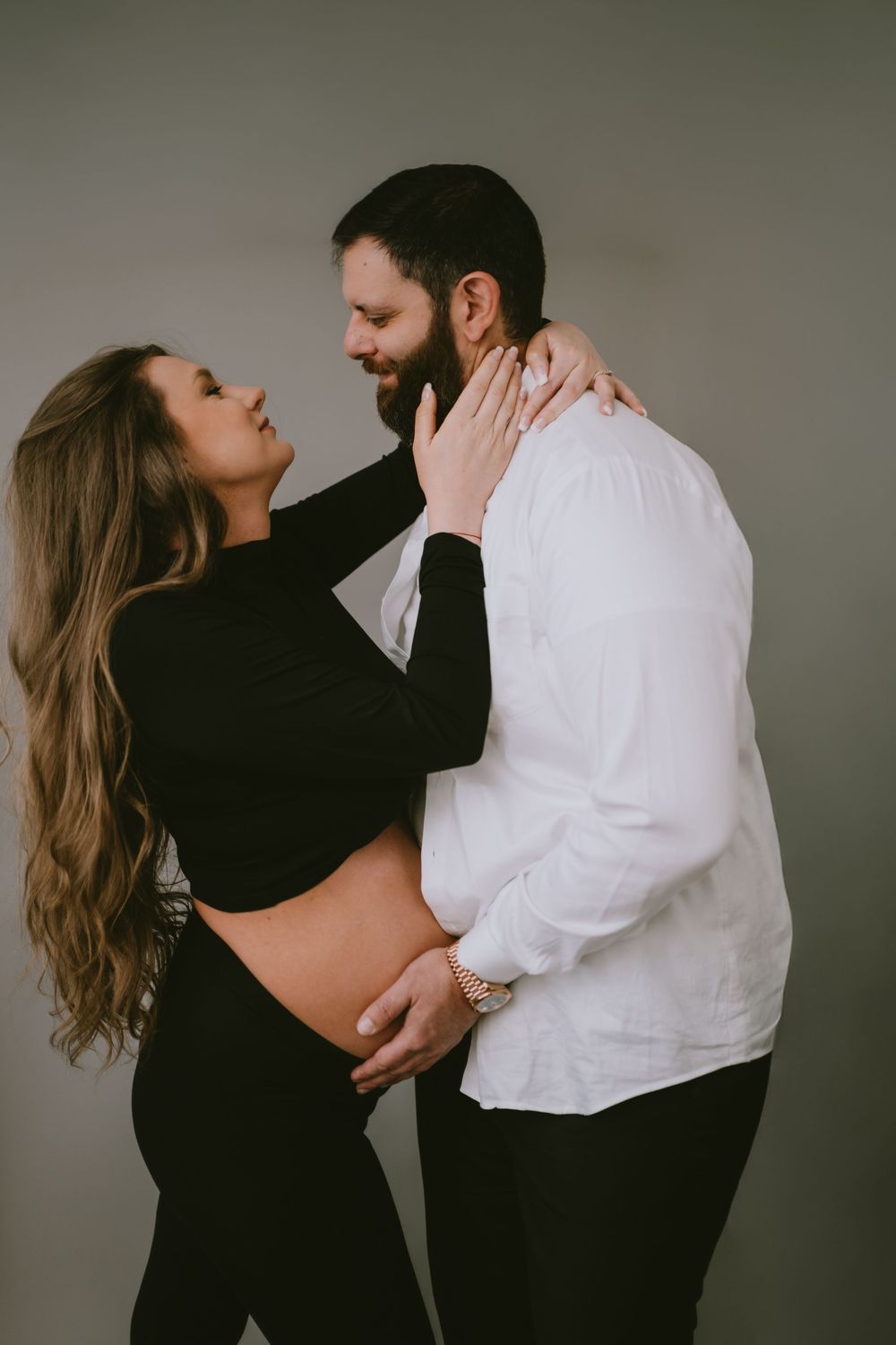 Couple sharing an intimate moment, pregnant woman in black crop top with partner in white shirt embracing her baby bump.