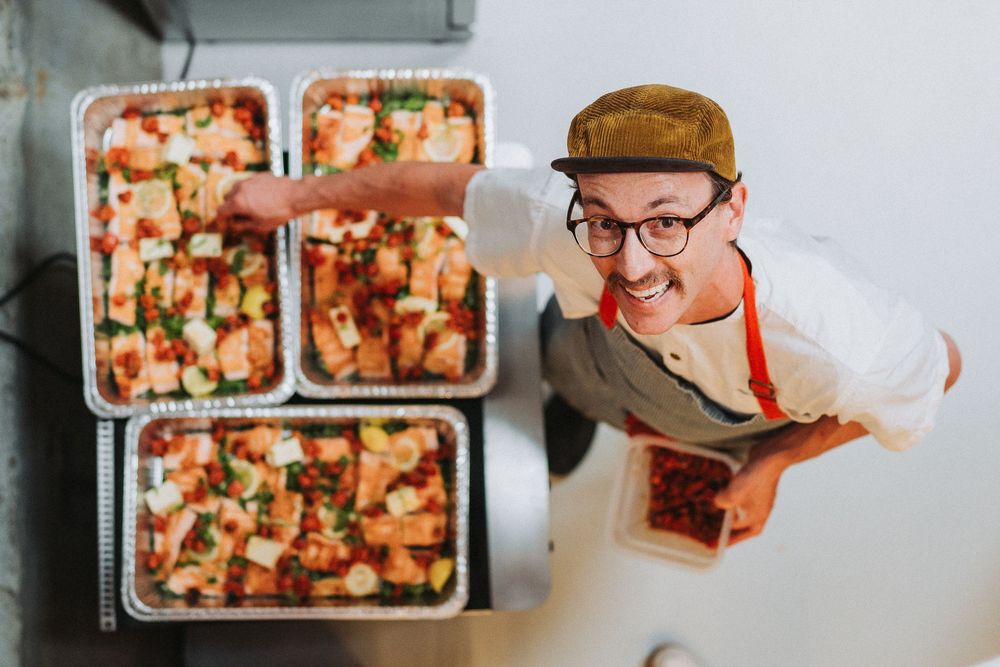 Smiling chef presenting trays of prepared salmon dishes from overhead perspective.