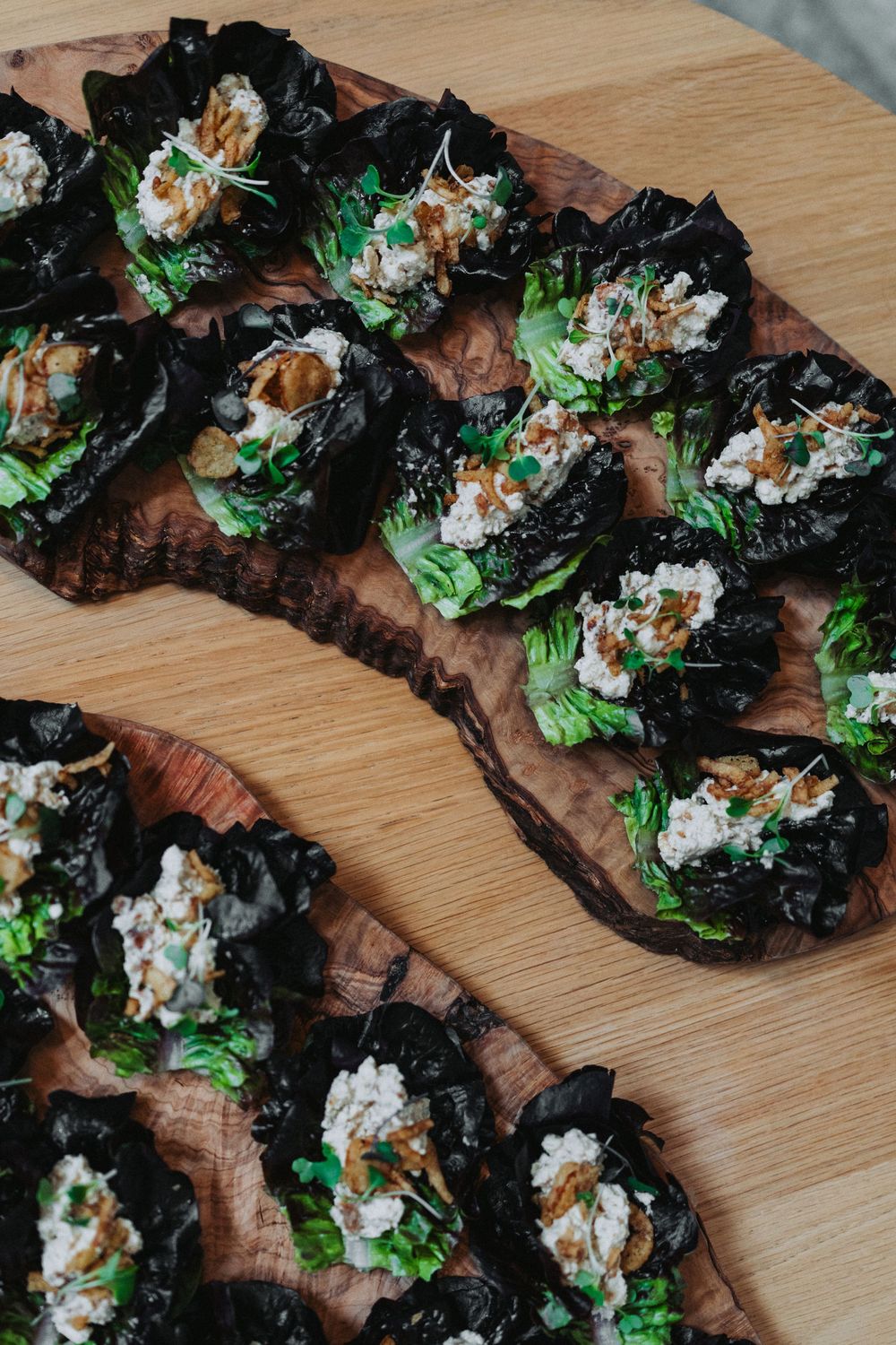 Elegant appetizers with dark lettuce cups filled with chicken salad on wooden board.
