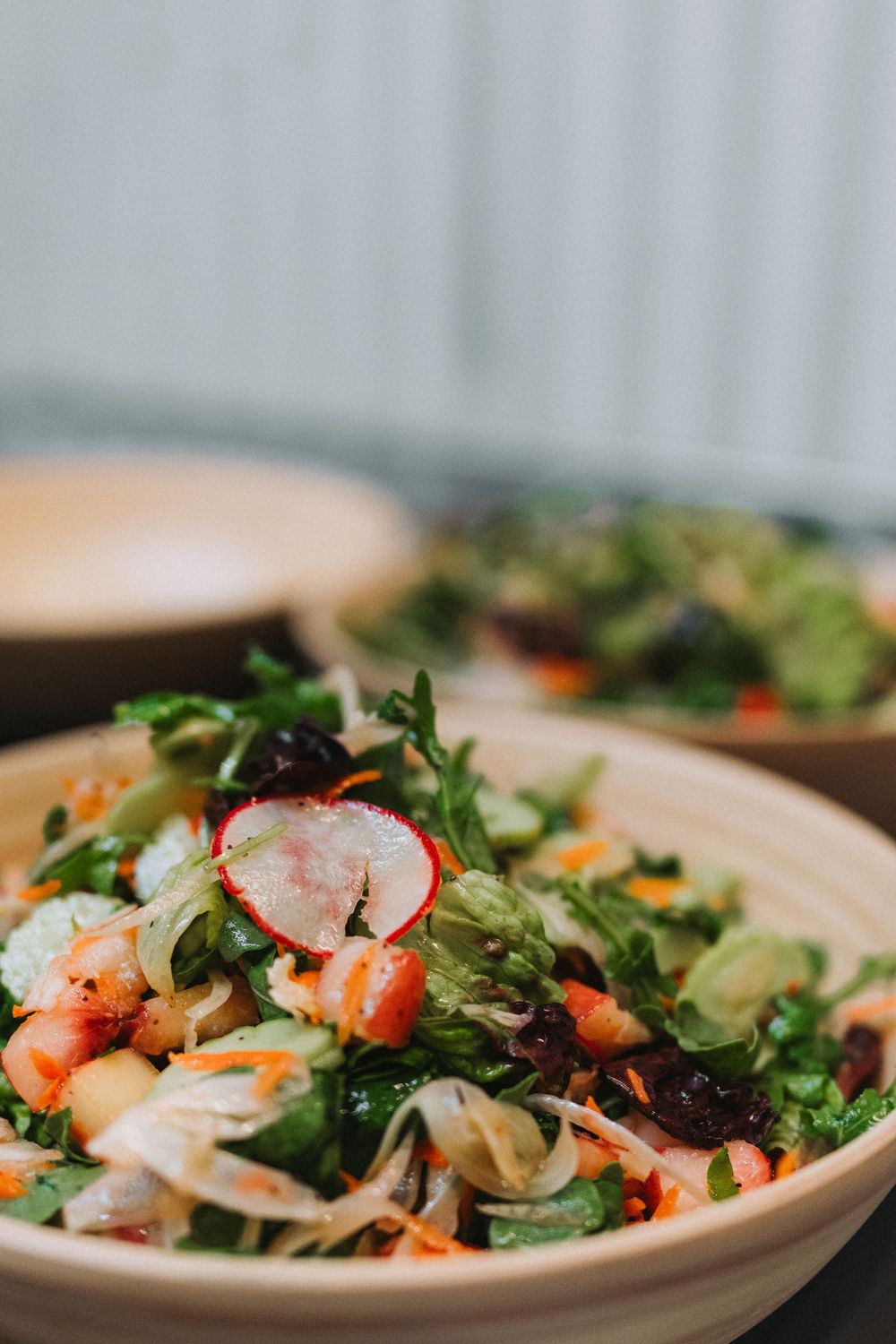 Fresh colorful salad with radishes, chickpeas, carrots, and greens served in a wooden bowl.