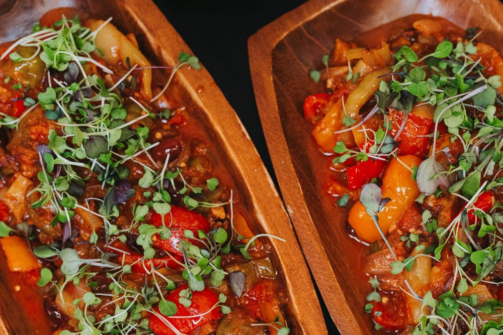 Two wooden serving dishes filled with roasted vegetables and cherry tomatoes topped with microgreens.