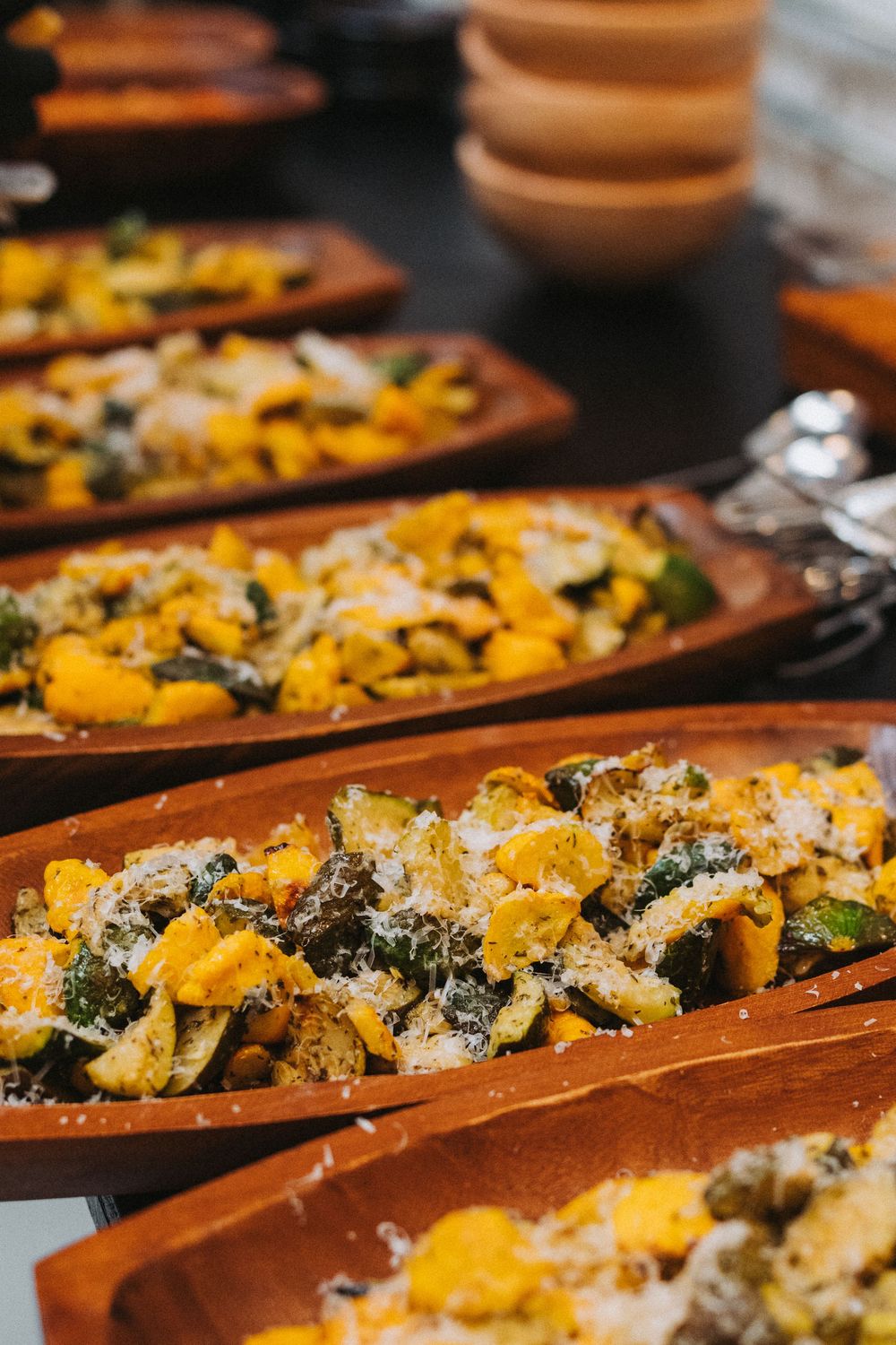 Roasted butternut squash and zucchini topped with grated parmesan cheese in wooden serving dishes.