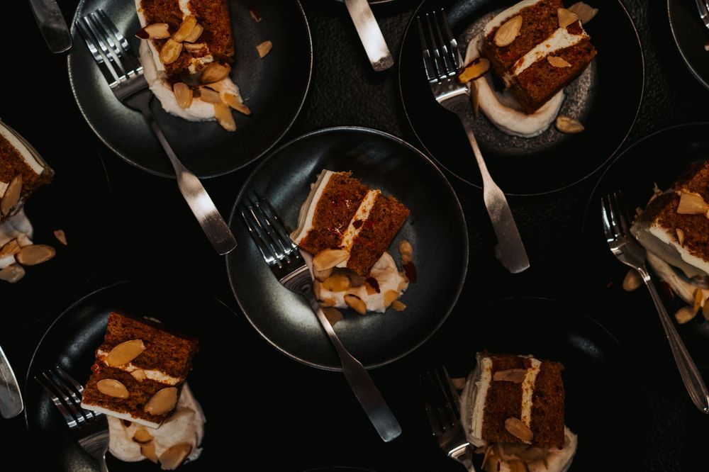 Overhead view of sliced carrot cake with cream cheese frosting served on dark plates with forks.