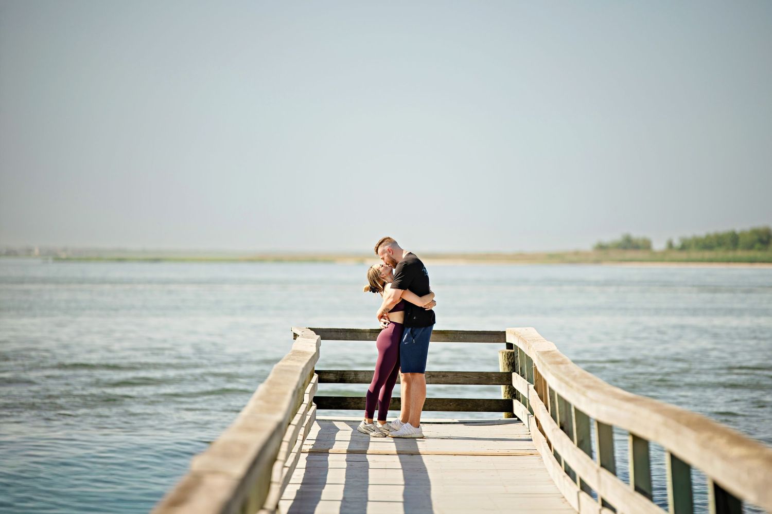 A couple embraces lovingly on a dirt path beside tall ornamental grasses on an overcast afternoon.