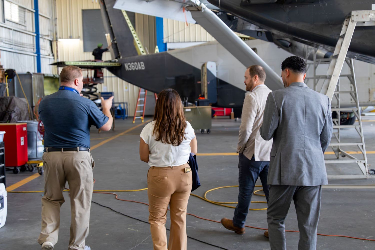Group of professionals touring a military aircraft hangar, examining a jet up close.