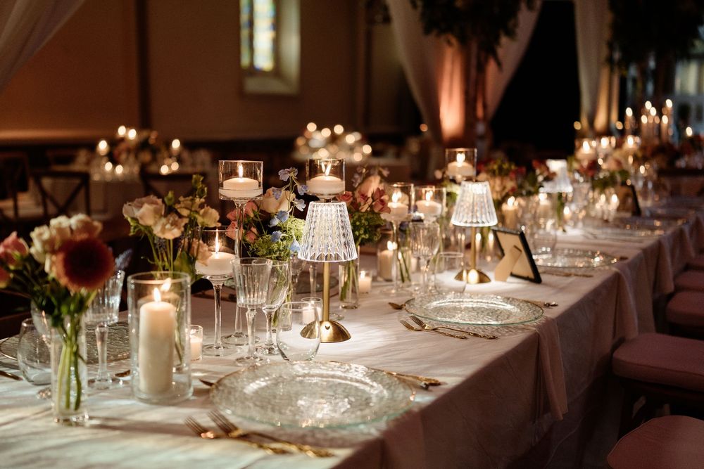 Elegant wedding reception table set with candles, crystal holders, floral arrangements, and fine glassware in a warmly lit venue.