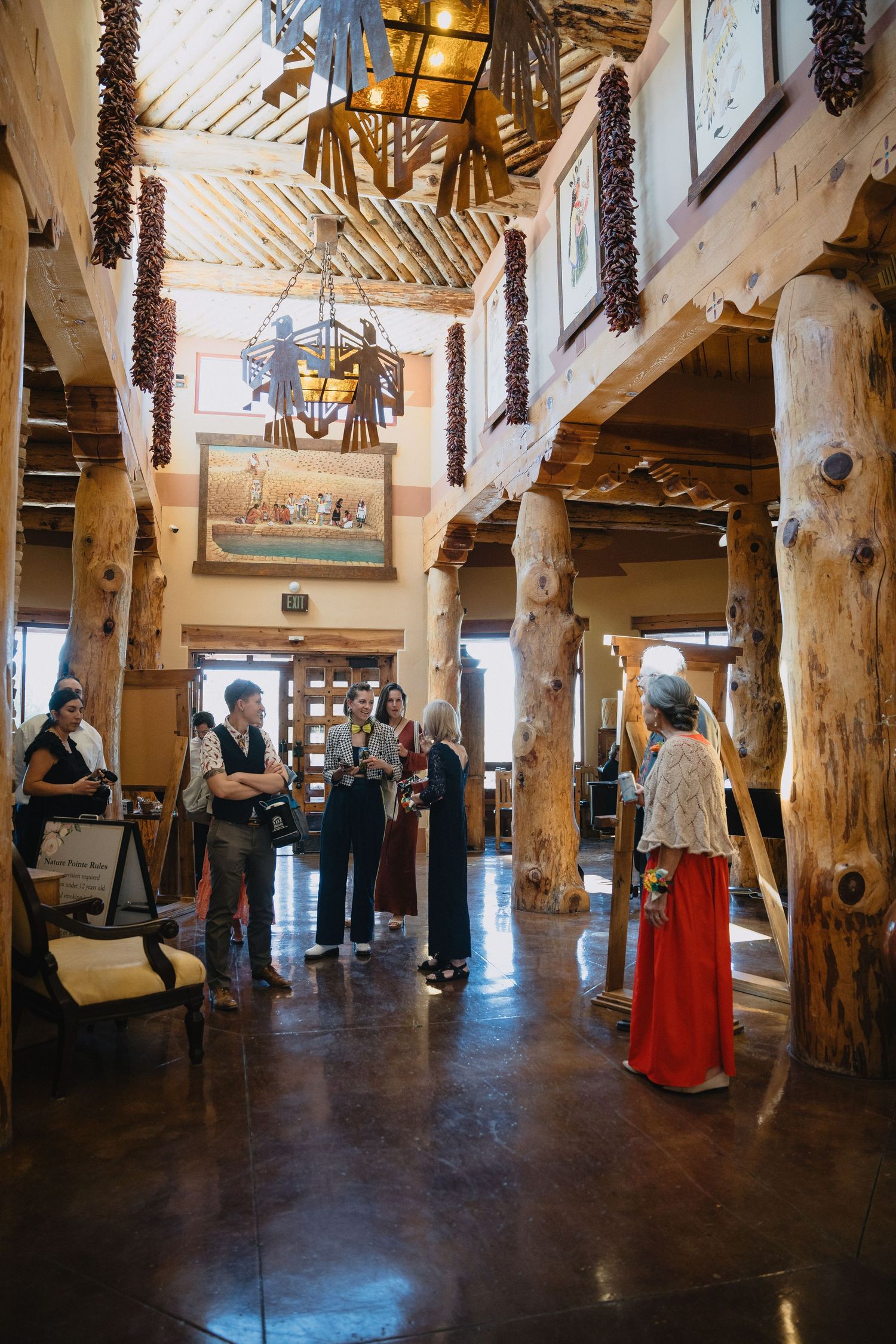Wedding guests mingling in rustic Southwestern lodge lobby with log columns and hanging chili ristras.