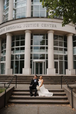 Bride and groom sitting on steps outside the Leno Regional Justice Center in wedding attire.