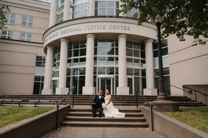 Bride and groom sitting on steps outside Hillis Regional Justice Center building with large columns.