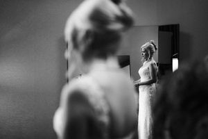 Black and white photo of a bride in a lace wedding dress admiring her reflection in a mirror.