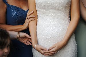 Bride in a white sequined wedding gown being helped by a woman in a blue dress.