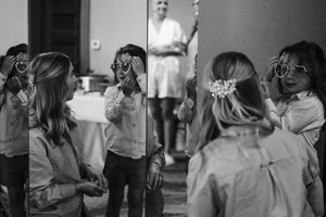 Black and white photo of girls wearing heart-shaped sunglasses, reflected in a mirror at a wedding celebration.