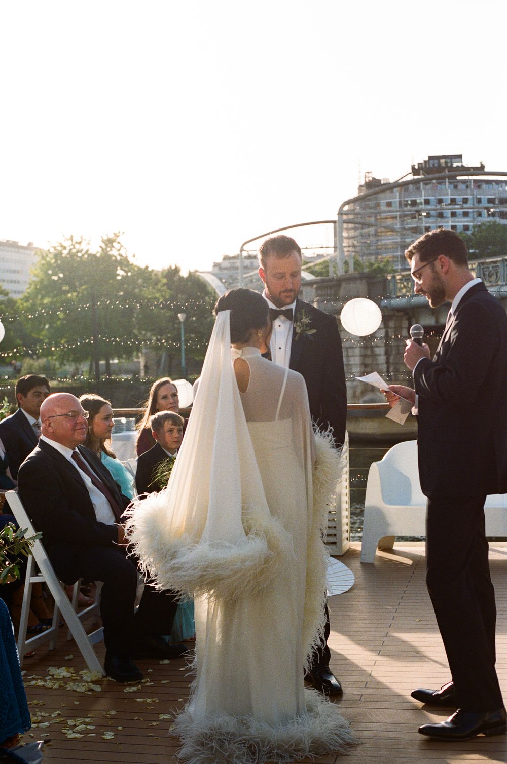 Bride in feather cape veil and groom exchange vows at outdoor rooftop wedding ceremony at golden hour. paris wedding photographer, film