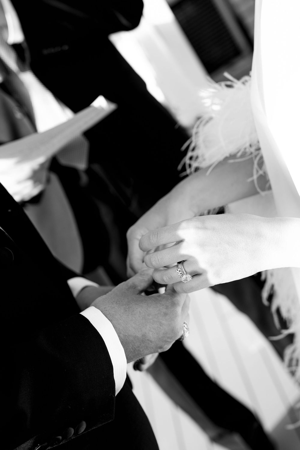 Black and white photo of groom placing wedding ring on bride's finger during ceremony. Paris wedding photographer, cinematic