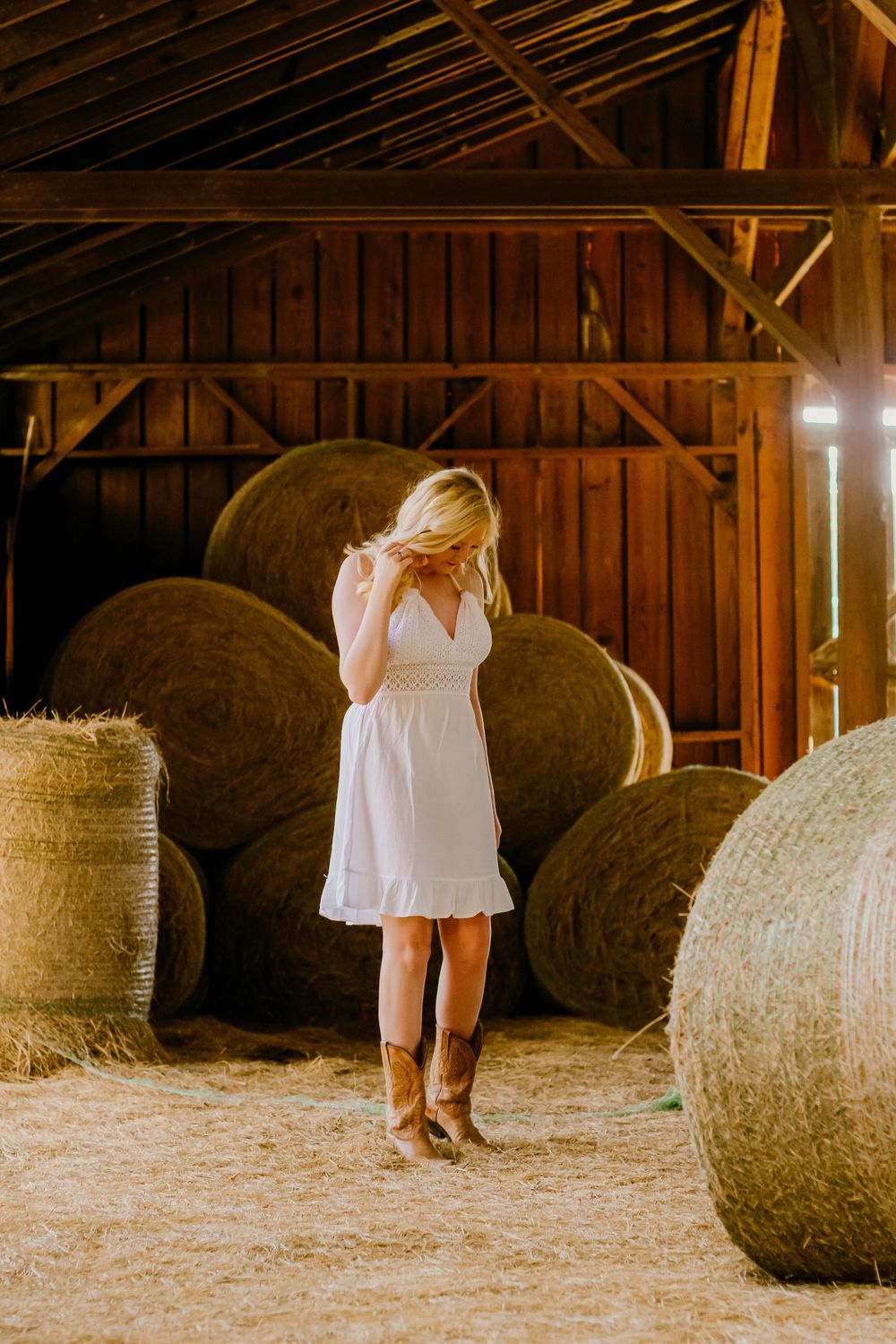 A white sundress contrasts beautifully with rustic hay bales inside a wooden barn.