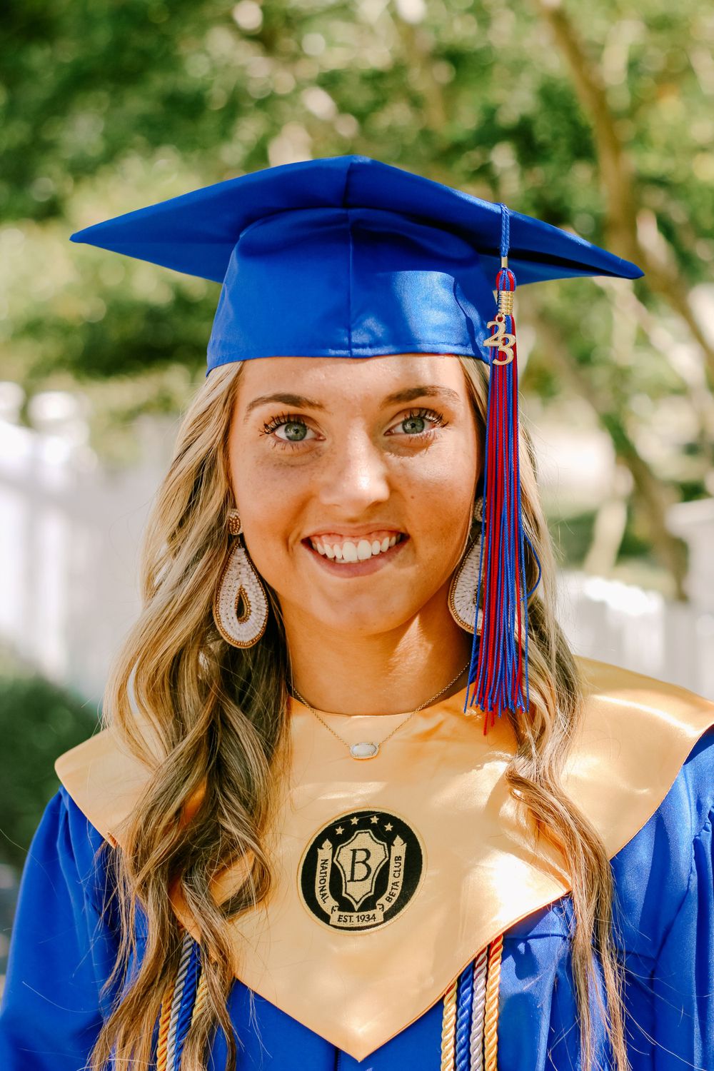 A graduate wearing blue cap and gown with gold stole poses for graduation photos.