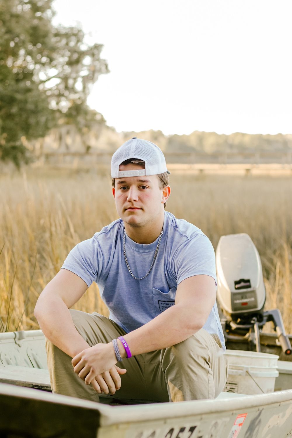 Casual senior portrait of someone in a baseball cap sitting in a small fishing boat at sunset.