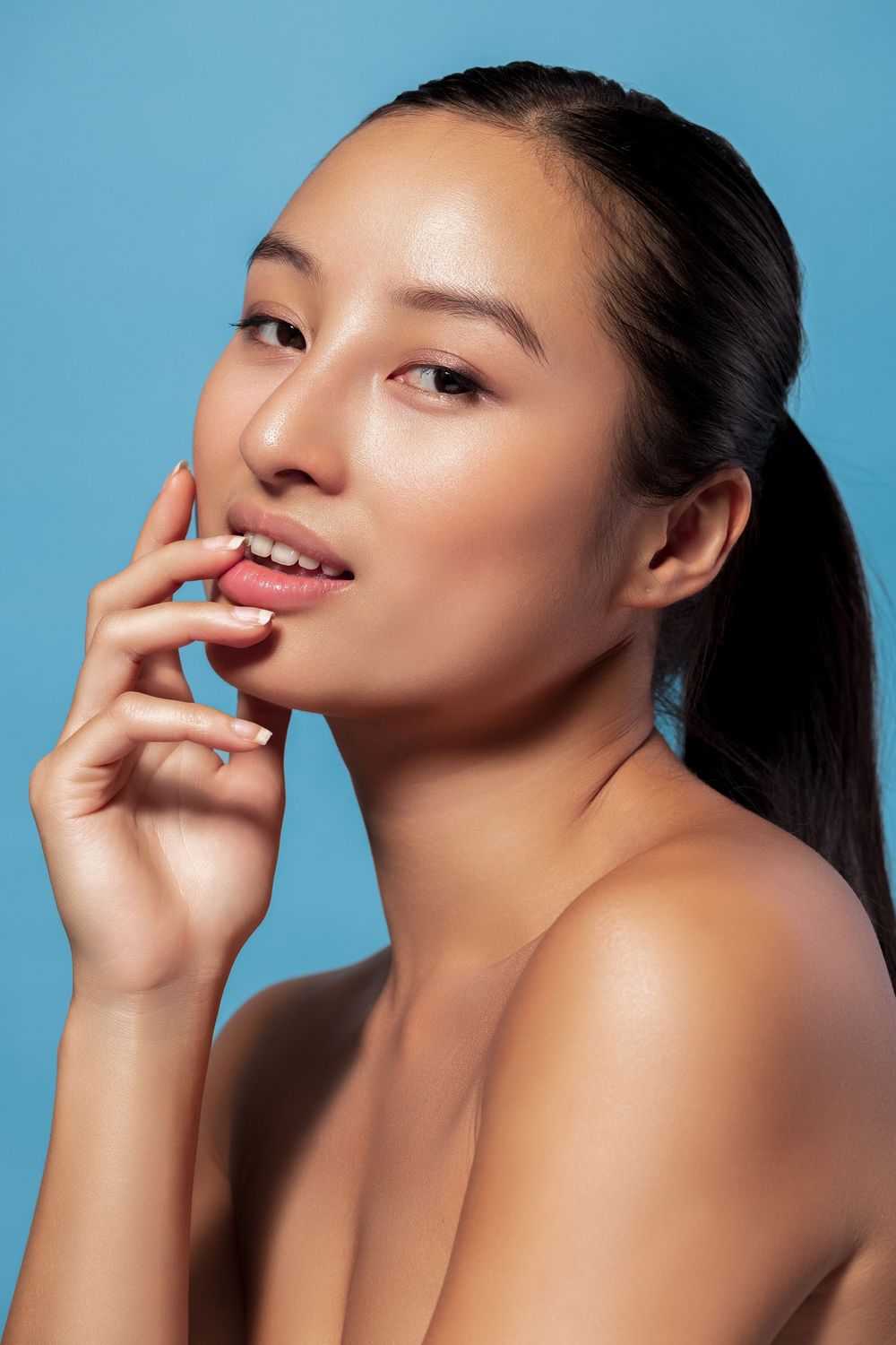 Beauty portrait against blue background showcasing natural makeup and glowing skin.