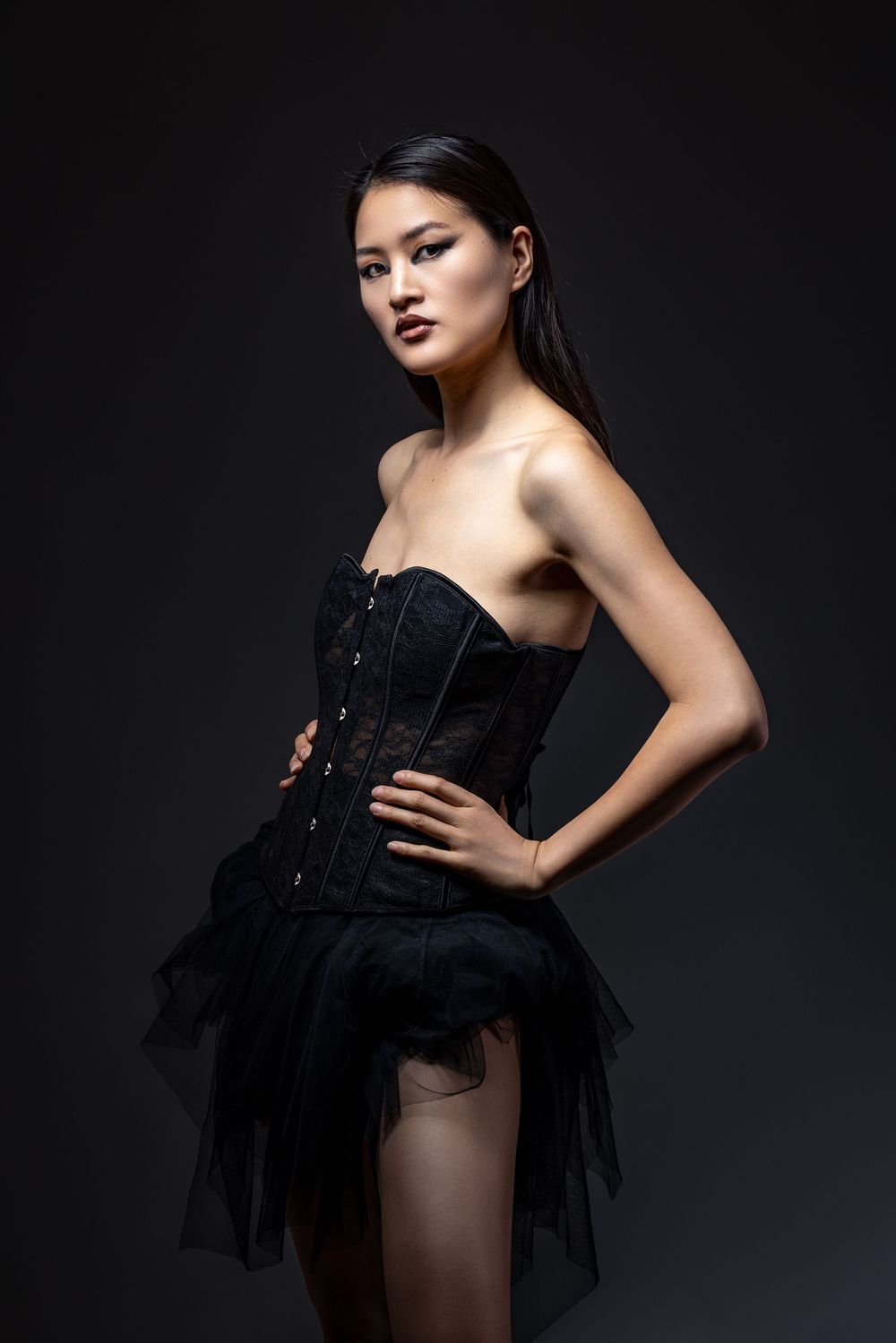 A dramatic fashion photo series featuring a model in a black corset dress against a dark background.