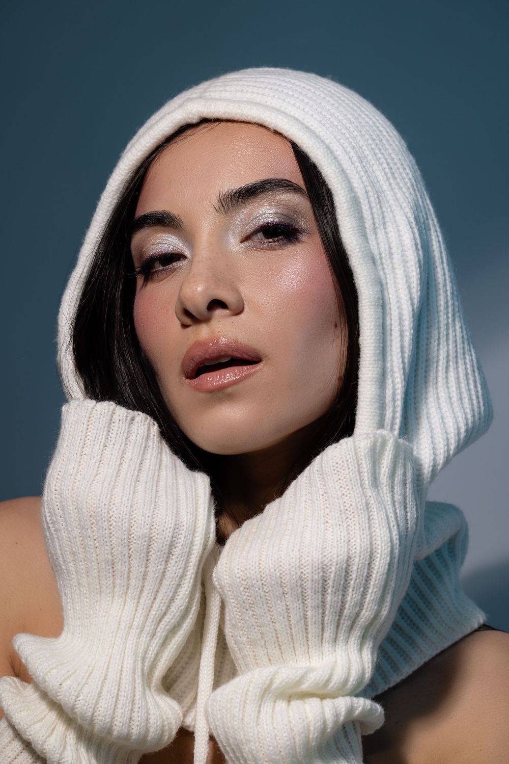 Fashion portrait featuring white knit turtleneck sweater and matching winter hat against blue background.