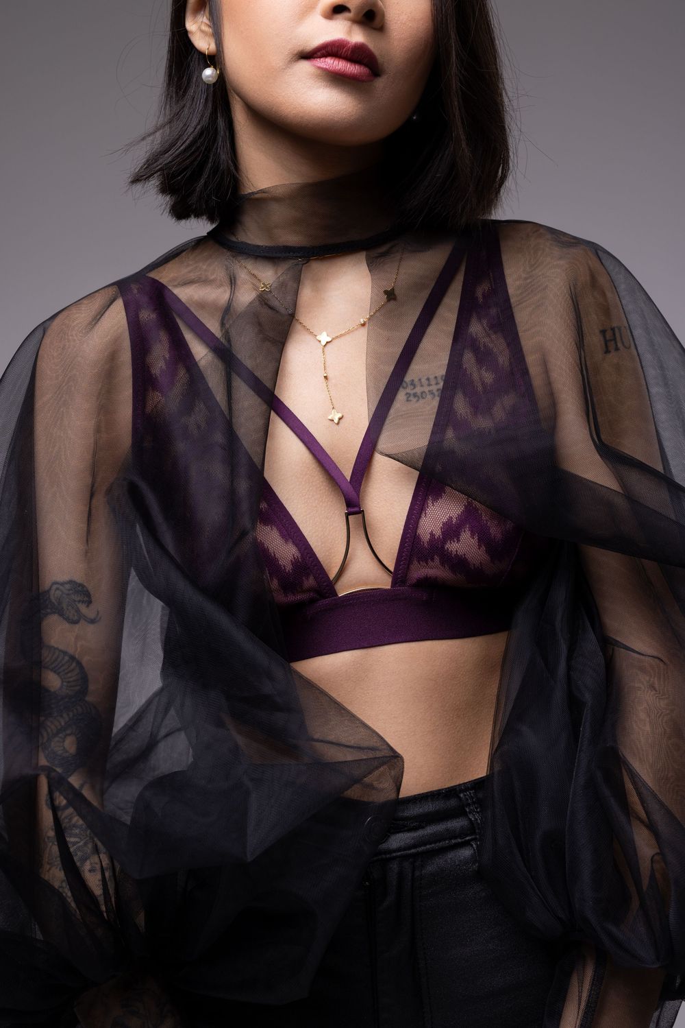 Fashion portrait showing purple lingerie bralette layered under sheer black mesh top with delicate necklace detail.