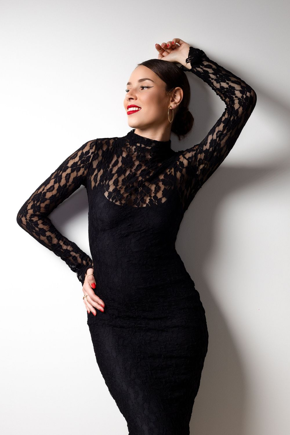Elegant black lace dress with long sleeves shown in fashionable pose against white wall.
