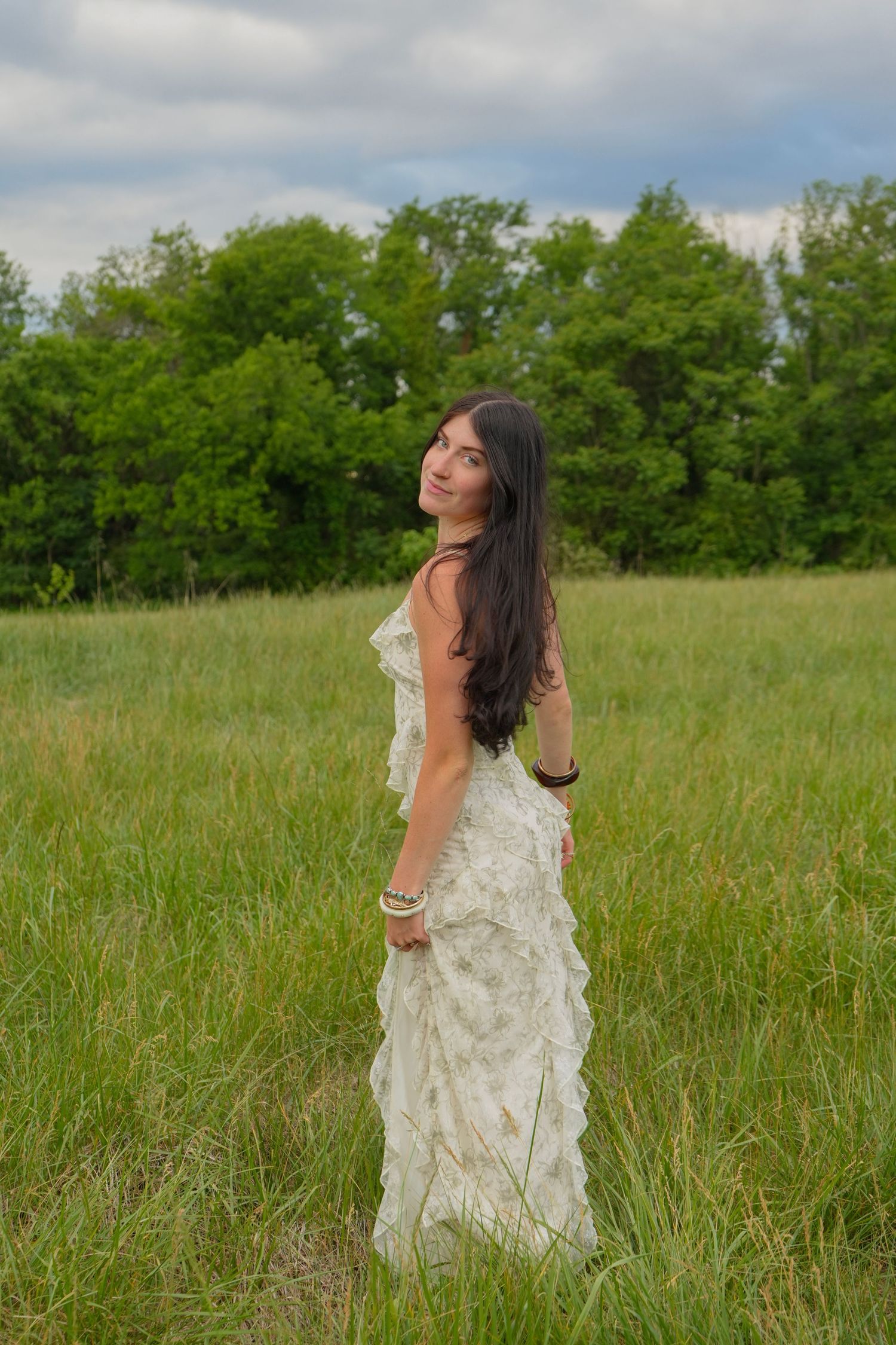 Young woman in white ruffled dress standing in green meadow looking back over her shoulder.
