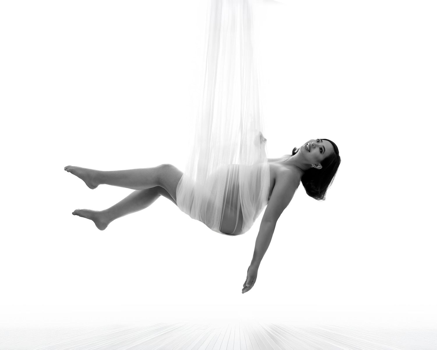 Expectant mother black and white photo sitting elegantly hanging from a white net in studio.