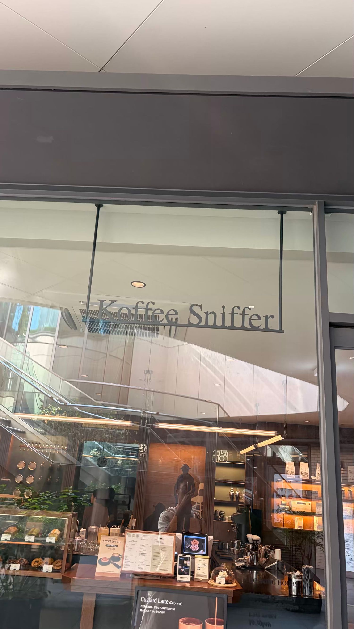 Interior view of Koffee Sniffer cafe through glass storefront, featuring warm lighting and coffee equipment display.