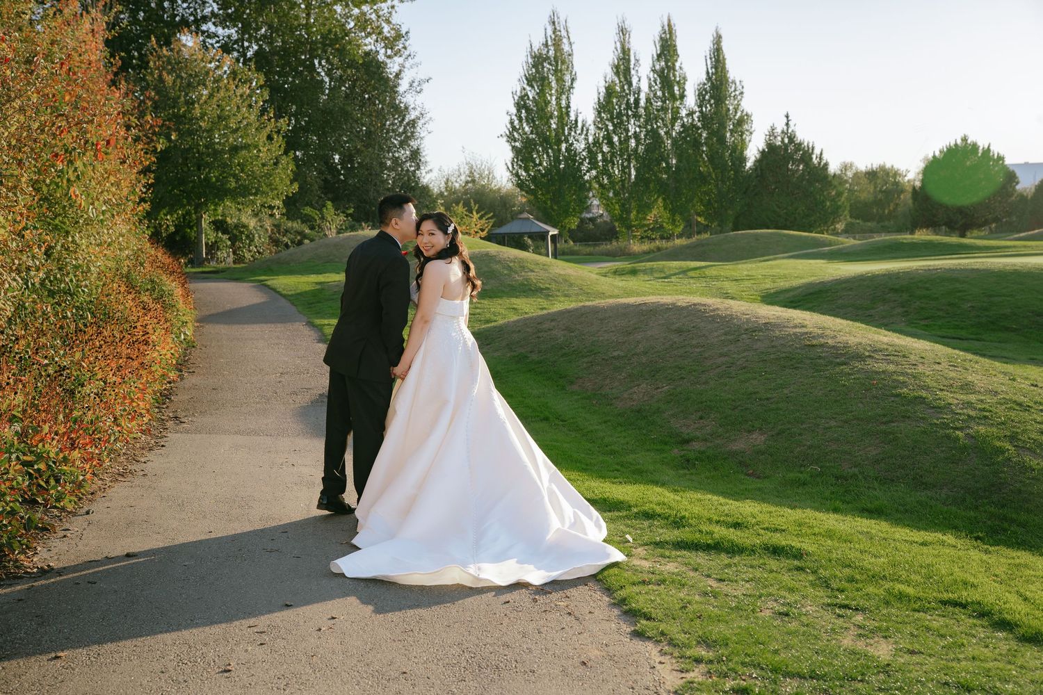 Riley kissing Jennifer's cheek on a golf course path at Riverway Clubhouse during their wedding portraits in Burnaby
