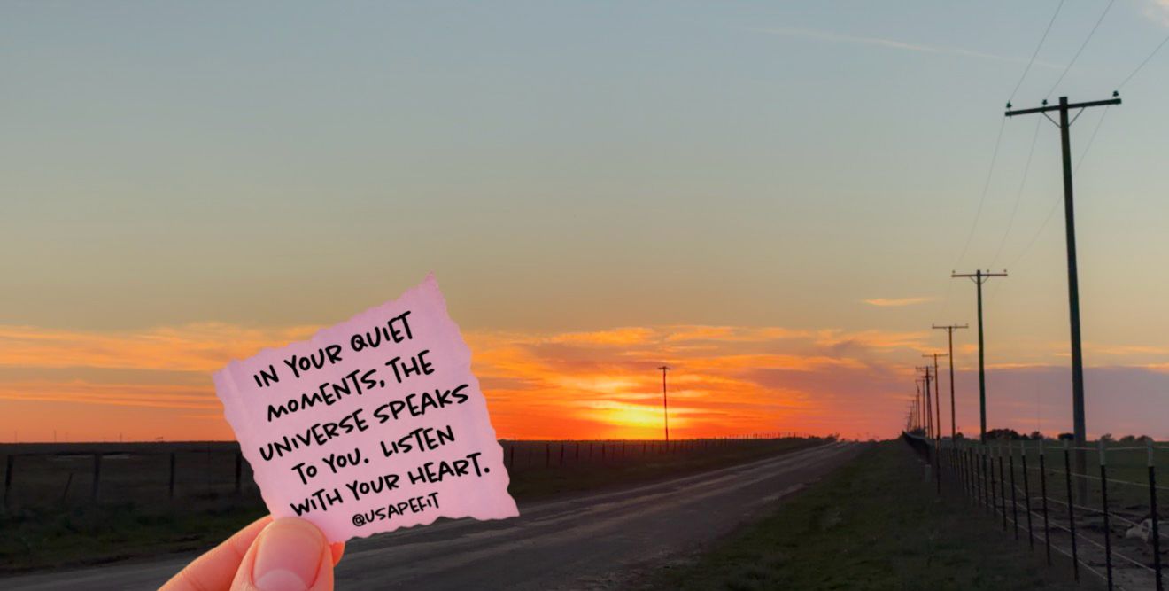 Hand holding a note card with inspirational quote at sunset over a rural road with telephone poles.
