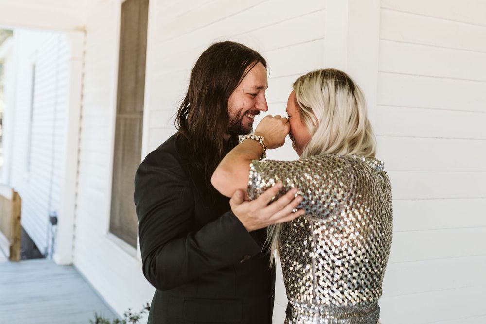 A couple shares a romantic moment, the woman in a silver sequin top and the man in black, smiling face-to-face outdoors.