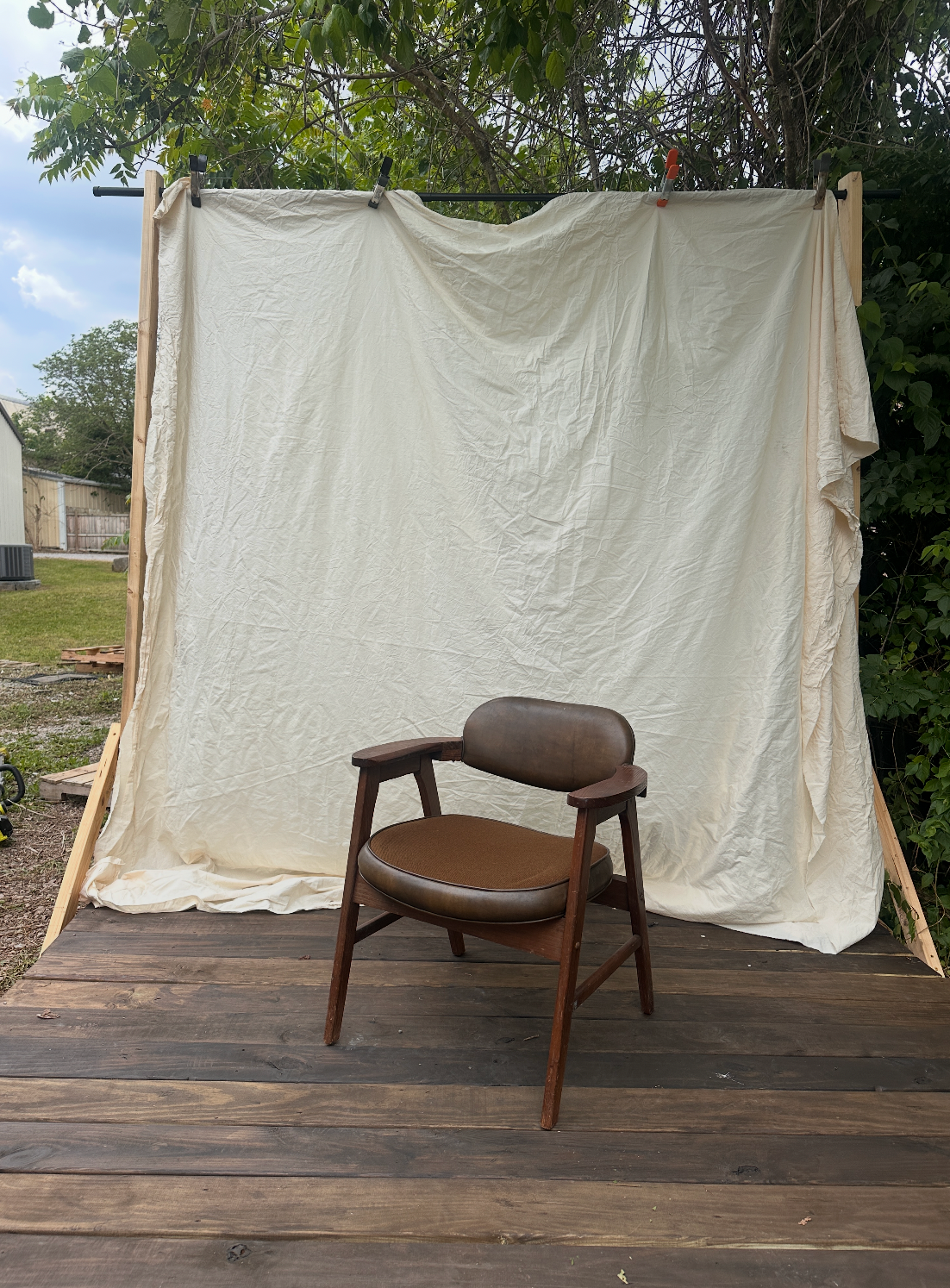 Mid-century modern brown leather chair on wood deck with cream fabric backdrop outdoors in photography studio