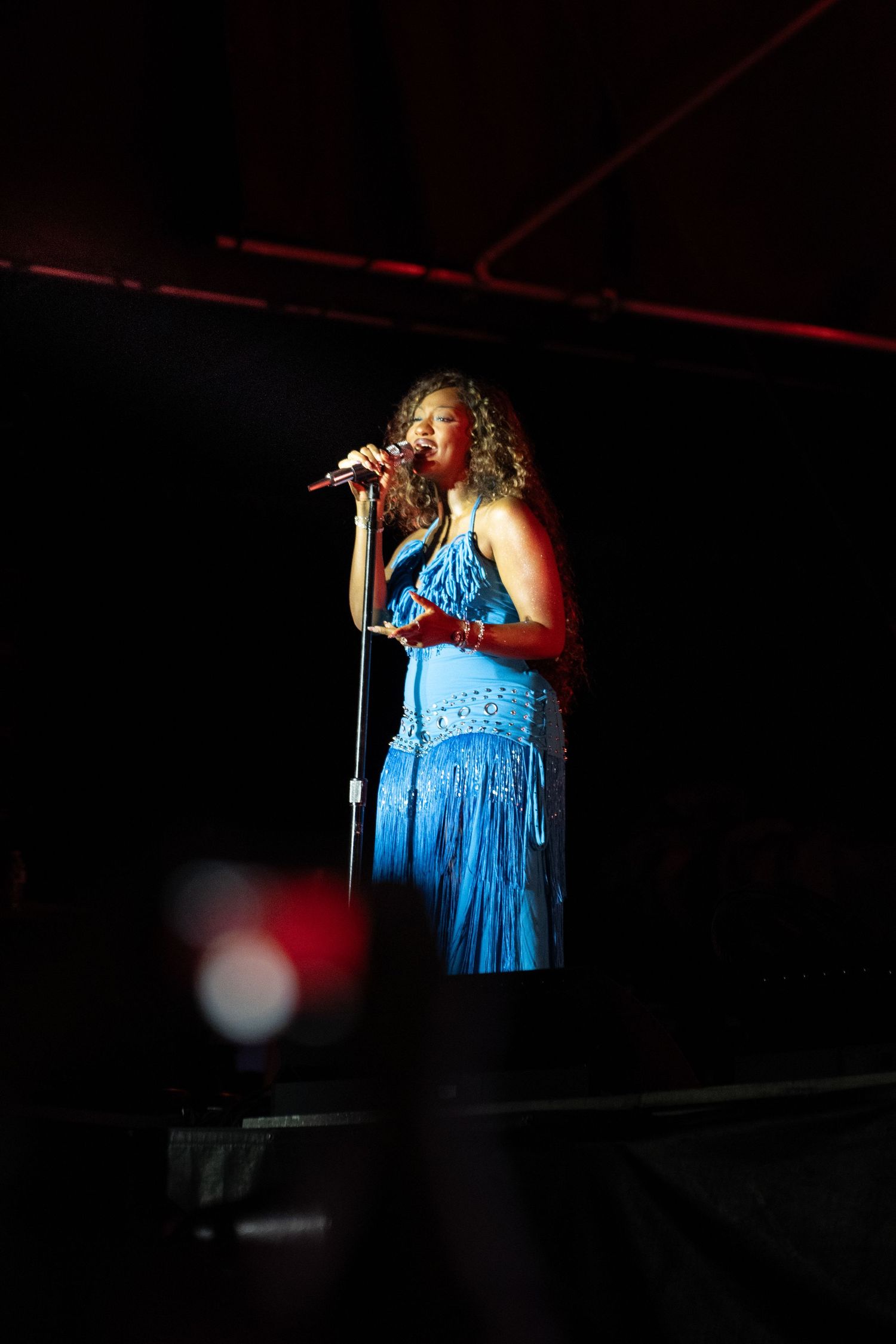 Woman in blue dress singing on stage with microphone under spotlight at live concert.