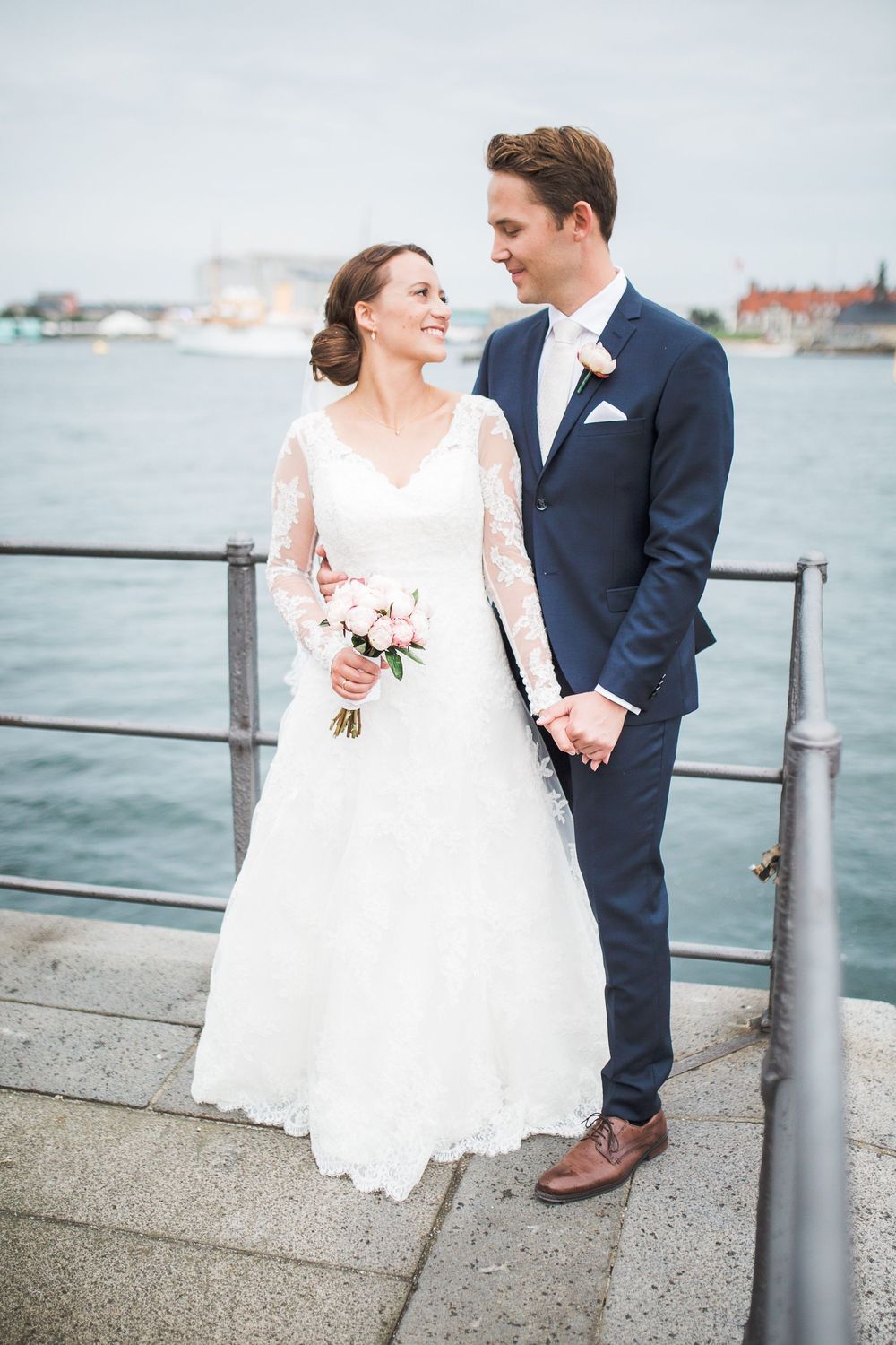 Brudepar ved vandet med havnen i baggrunden – bryllupsfoto af Martin & Louise