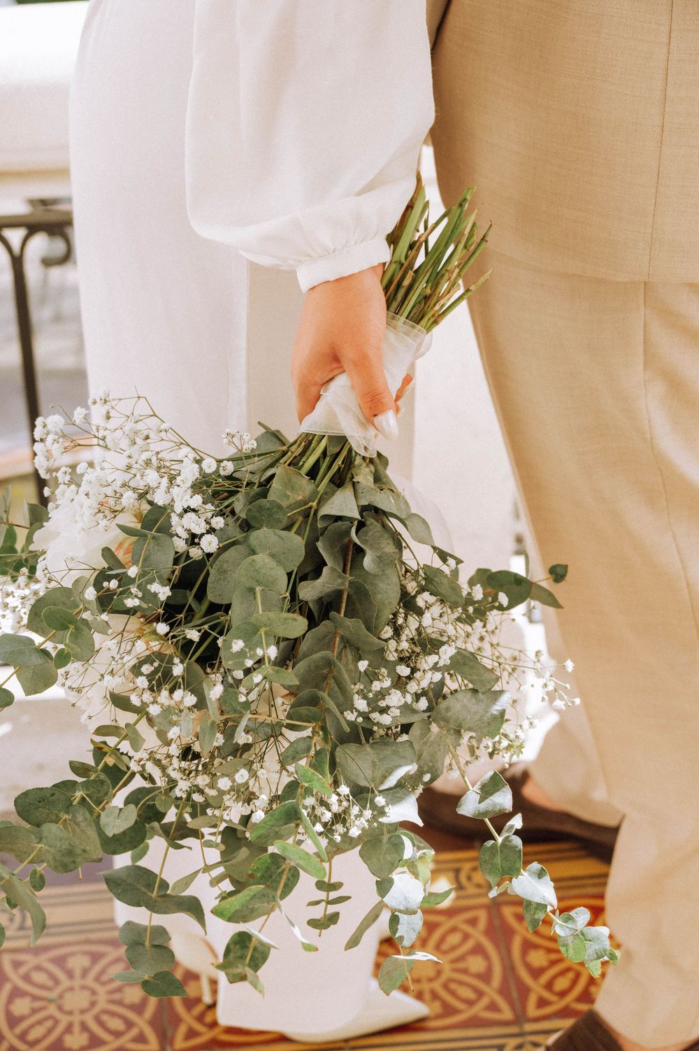 Bride holding a lush eucalyptus and baby's breath wedding bouquet wrapped in white ribbon at a ceremony.