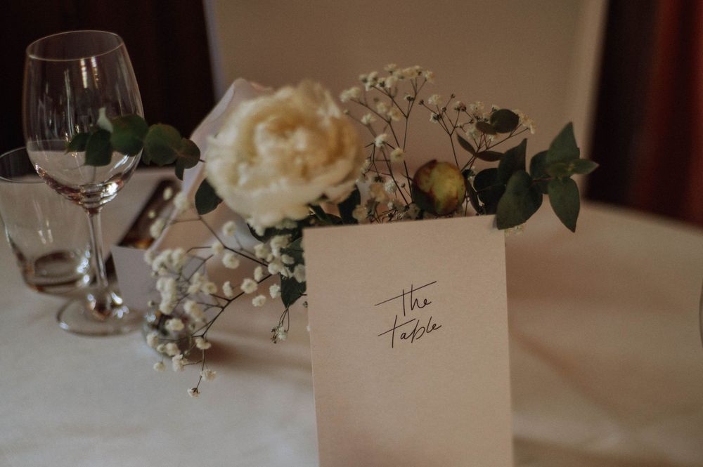 Elegant wedding table setting with white peony floral arrangement, baby's breath, and a calligraphy place card on white linen.