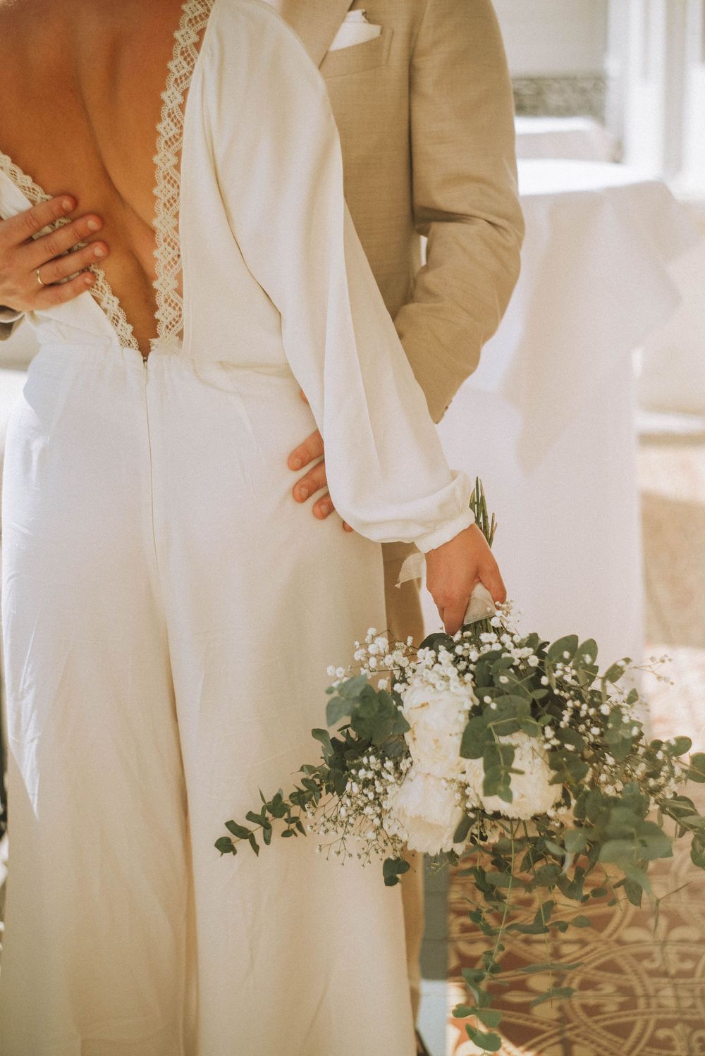 Bride in white dress holding eucalyptus bouquet stands beside groom in beige suit at elegant wedding ceremony at Schlosshotel Kommende Ramer