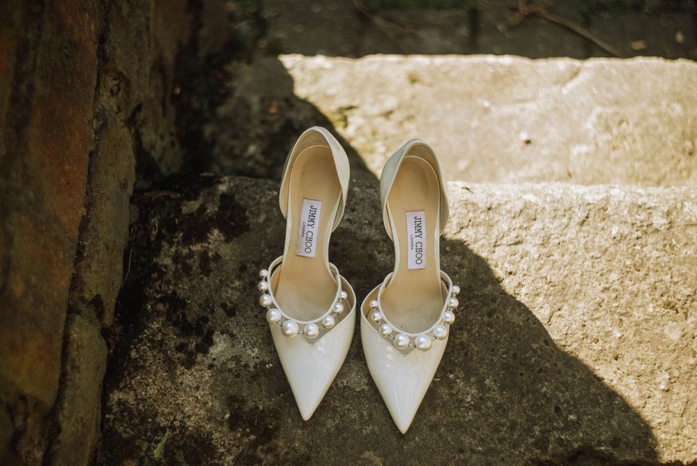 Elegant white pointed-toe Manolo Blahnik bridal heels with pearl embellishments resting on stone steps.