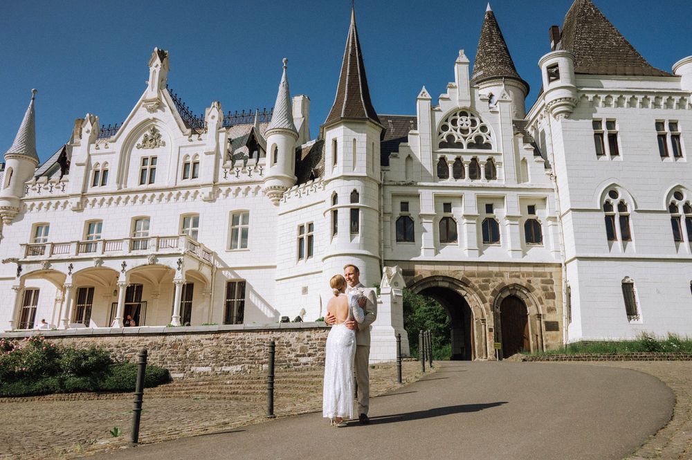 Bride and groom embracing in front of Schlosshotel Kommende Ramersdorf, Bonn in Bonn on a sunny wedding day.