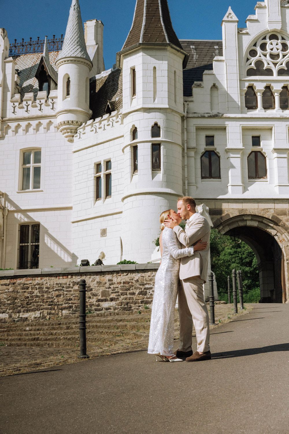 Bride and groom kissing in front of a stunning white castle venue on their wedding day.
