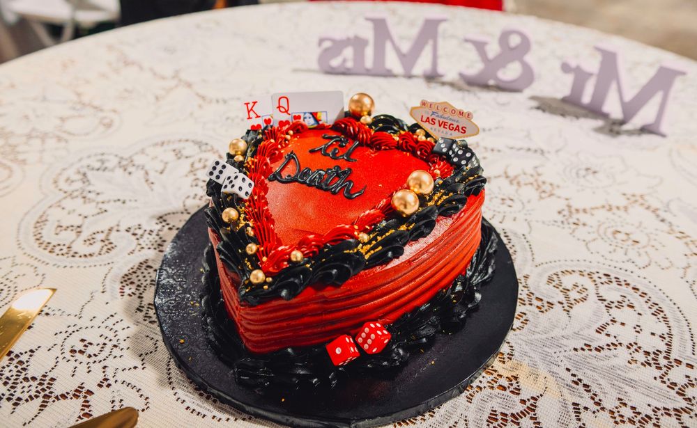 Red heart-shaped wedding cake with playing card decorations and gold accents on a lace tablecloth near Mr & Mrs sign.