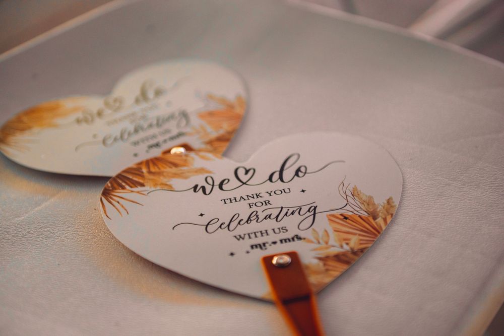 Heart-shaped wedding favor cards reading 'We Do, Thank You For Celebrating With Us' with golden floral accents.