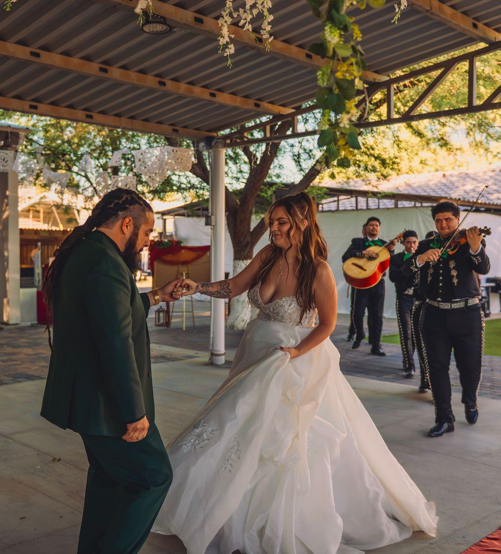 Bride and groom share first dance under pergola with mariachi band performing at outdoor wedding reception.