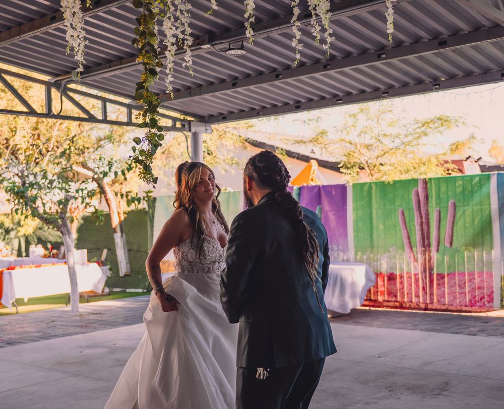 Bride and officiant stand together under decorated pavilion at outdoor wedding ceremony with colorful backdrop.
