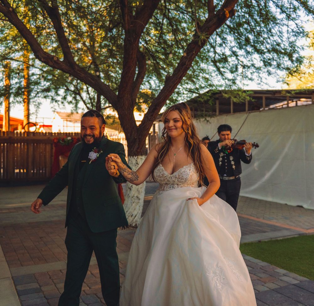 A bride and groom dance outdoors as a mariachi violinist performs at their wedding reception.