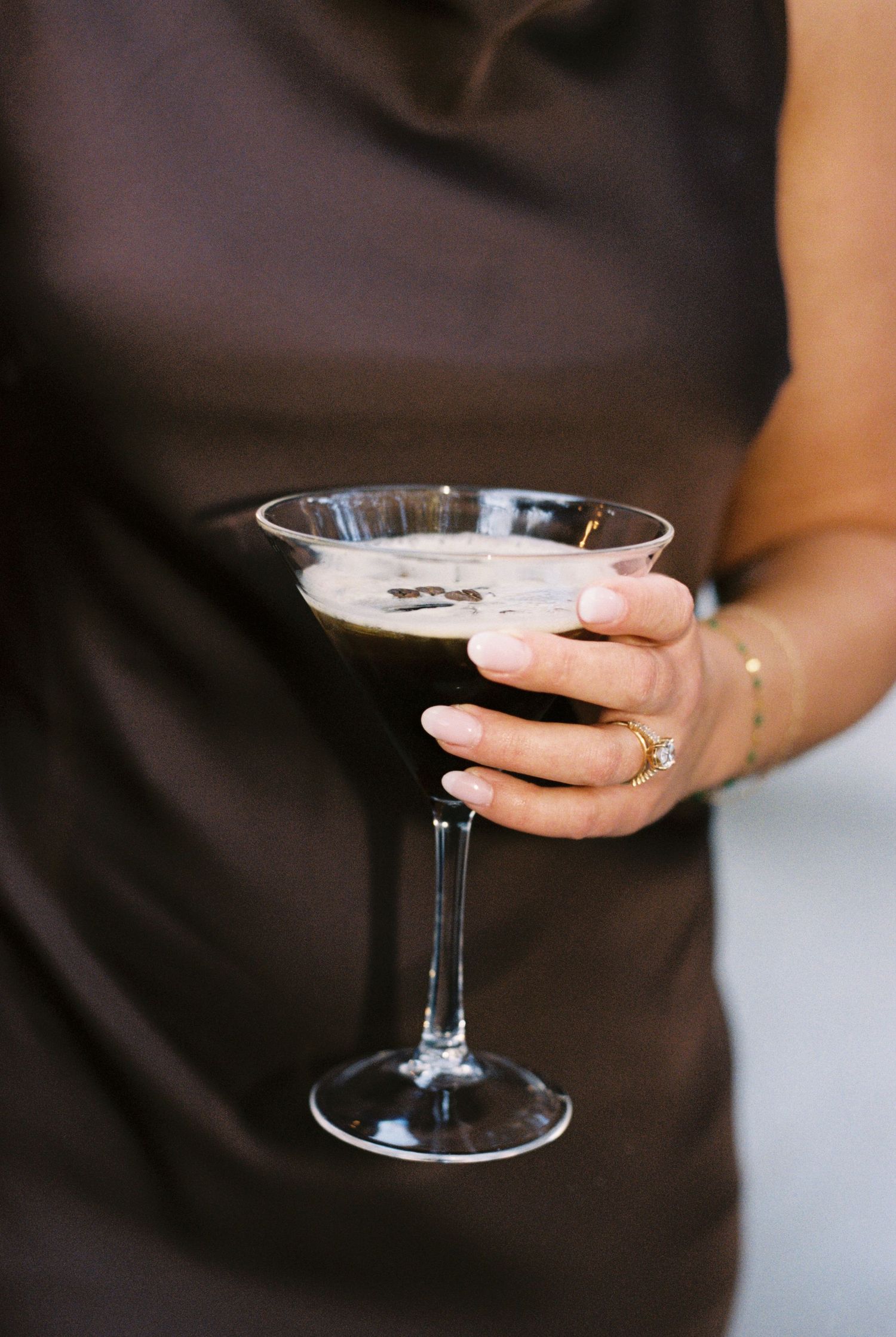 Woman in brown dress holding an espresso martini cocktail in a coupe glass during the reception at The Wildflower 301.
