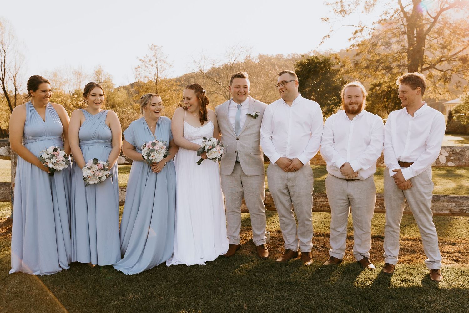 Wedding party group photo outdoors with light blue and neutral color scheme.