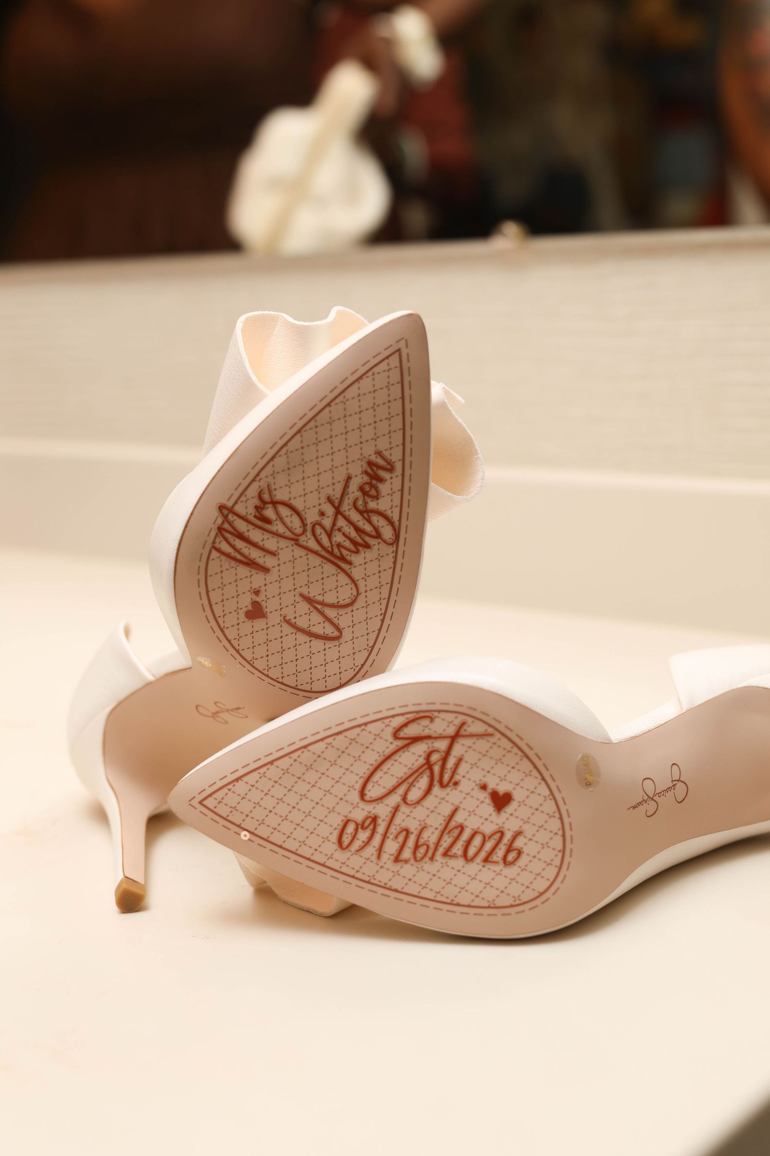 White bridal heels with custom soles reading Mrs. Whitson and Est. 09/26/2026, resting on a bathroom counter.